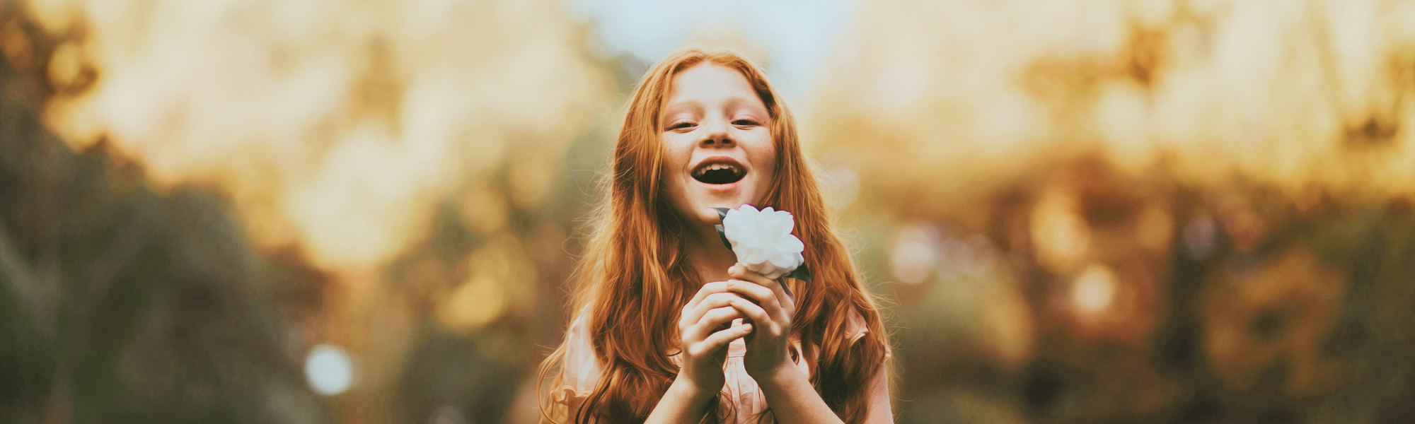 fillette souriante avec une fleur blanche représentant la connexion avec son enfant intérieur-programme Enfant Intérieur - HarmoniSens