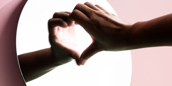 Mains formant un cœur sur son propre reflet dans un miroir, illustrant le miroir relationnel et l'importance de se reconnecter à soi plutôt que de chercher un sauveur extérieur — Harmoni’Sens.